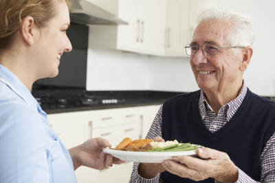 happy nurse giving food to elderly man